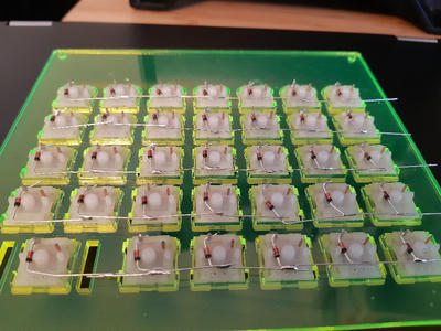 The underside of an acrylic plate for a custom mechanical keyboard showing the underside of the switches with diodes soldered to them, connecting the rows.