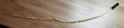 An intact yellow wire on a table with sections of insulation stripped off.