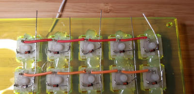 A close-up of 2 rows of mechanical keyswitches on the underside of a keyboard with the partially stripped wire connecting them.